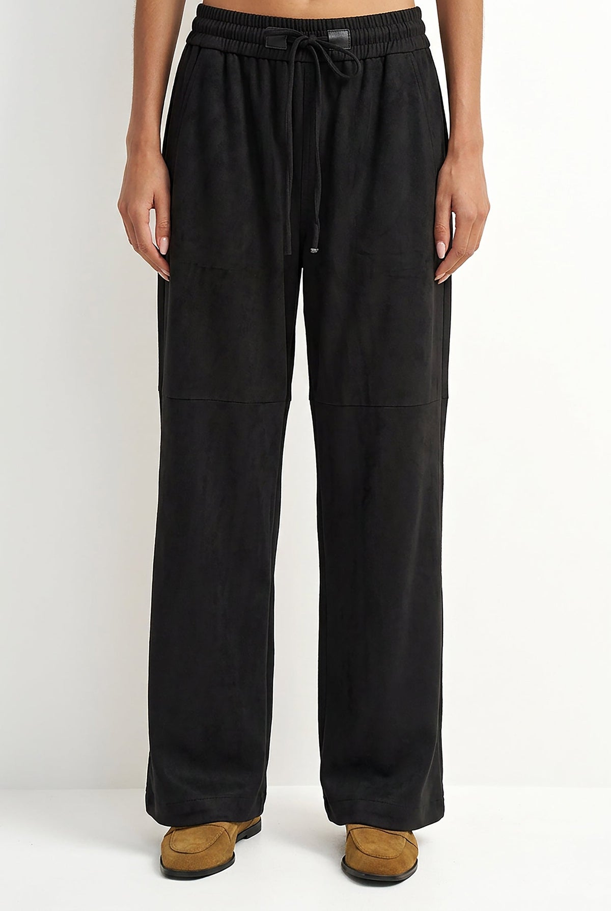 A person wearing black wide-leg drawstring pants and tan suede shoes, shown from the waist down against a plain light background.