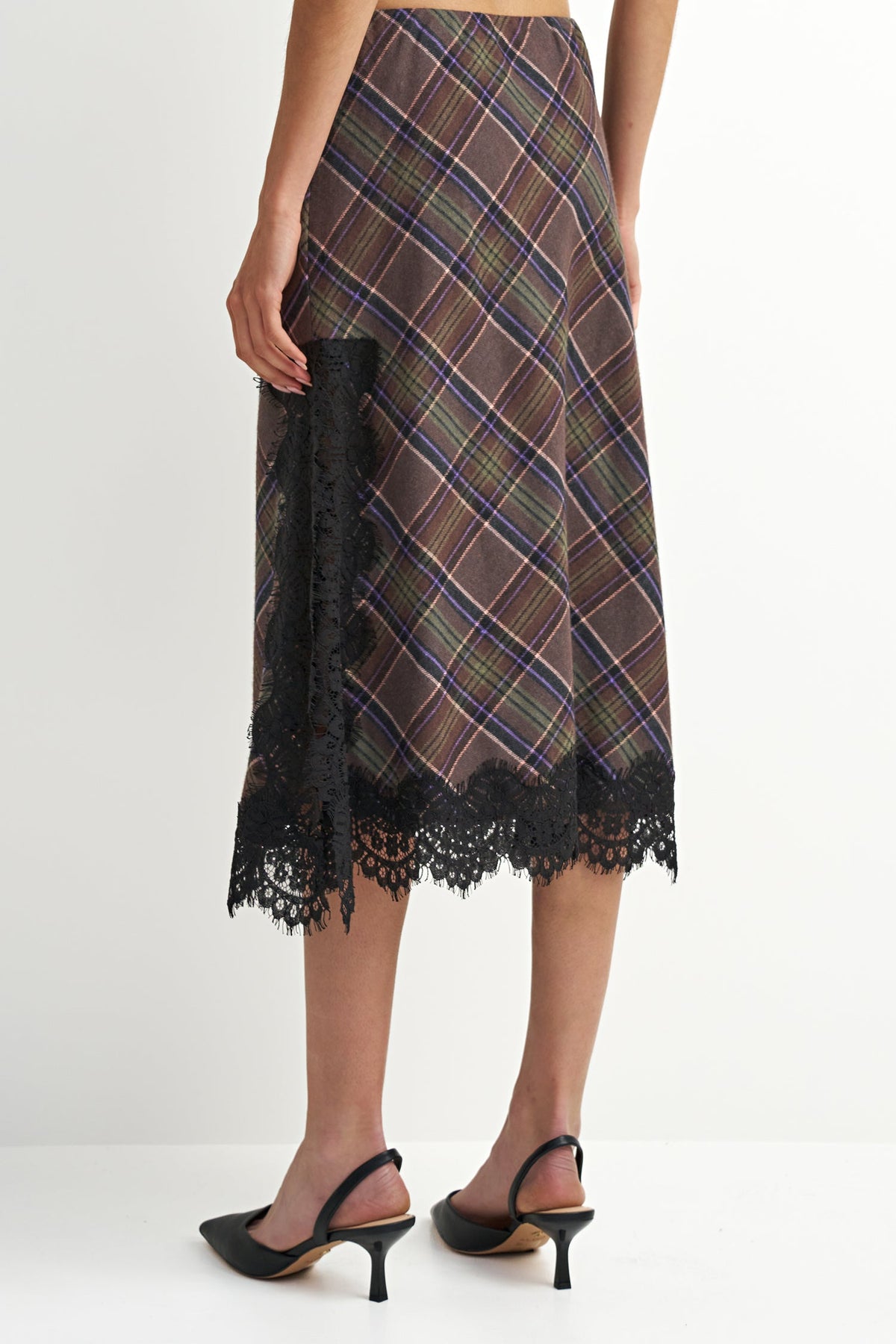 A model is shown from the back wearing a brown and navy plaid midi skirt with black lace trim, paired with black slingback heels.