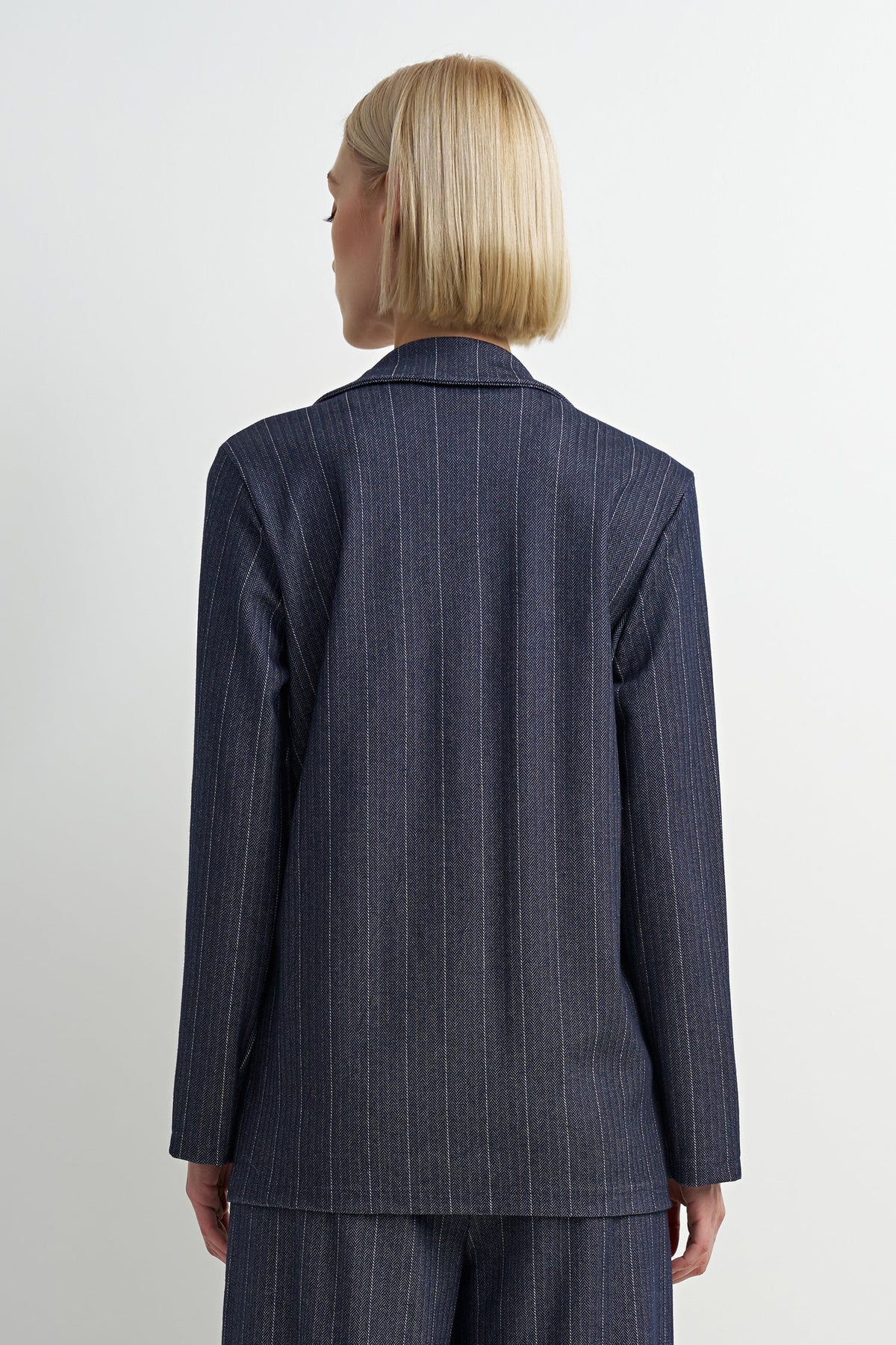 A model shown from the back wearing a navy blue pinstripe blazer and matching trousers against a plain white studio background.