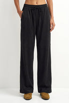 A person wearing black wide-leg drawstring pants with side pockets, paired with tan slip-on shoes, shown against a plain light gray studio background.