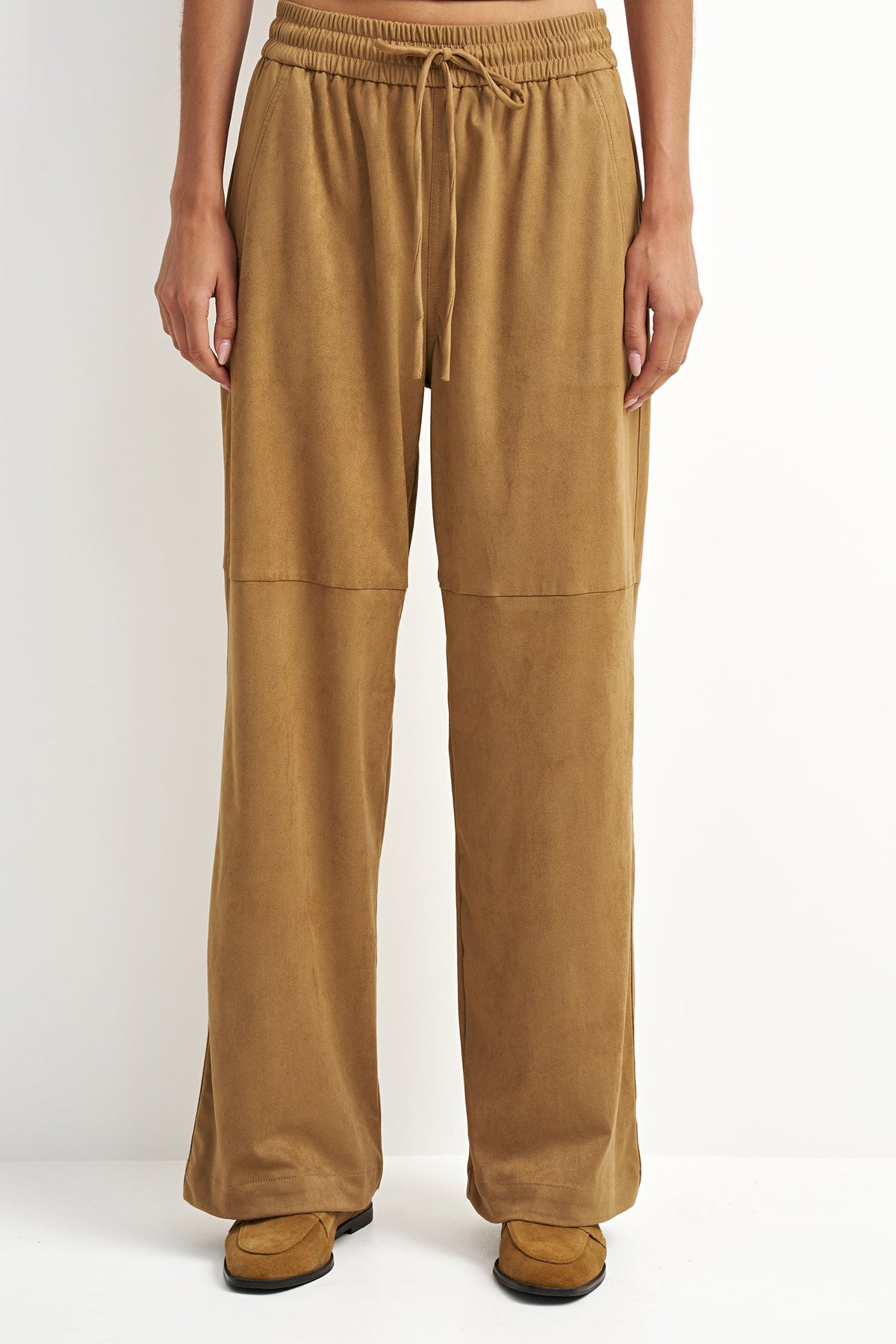 A person wearing wide-leg tan pants with an elastic drawstring waist and side pockets, shown from the waist down against a plain light background.