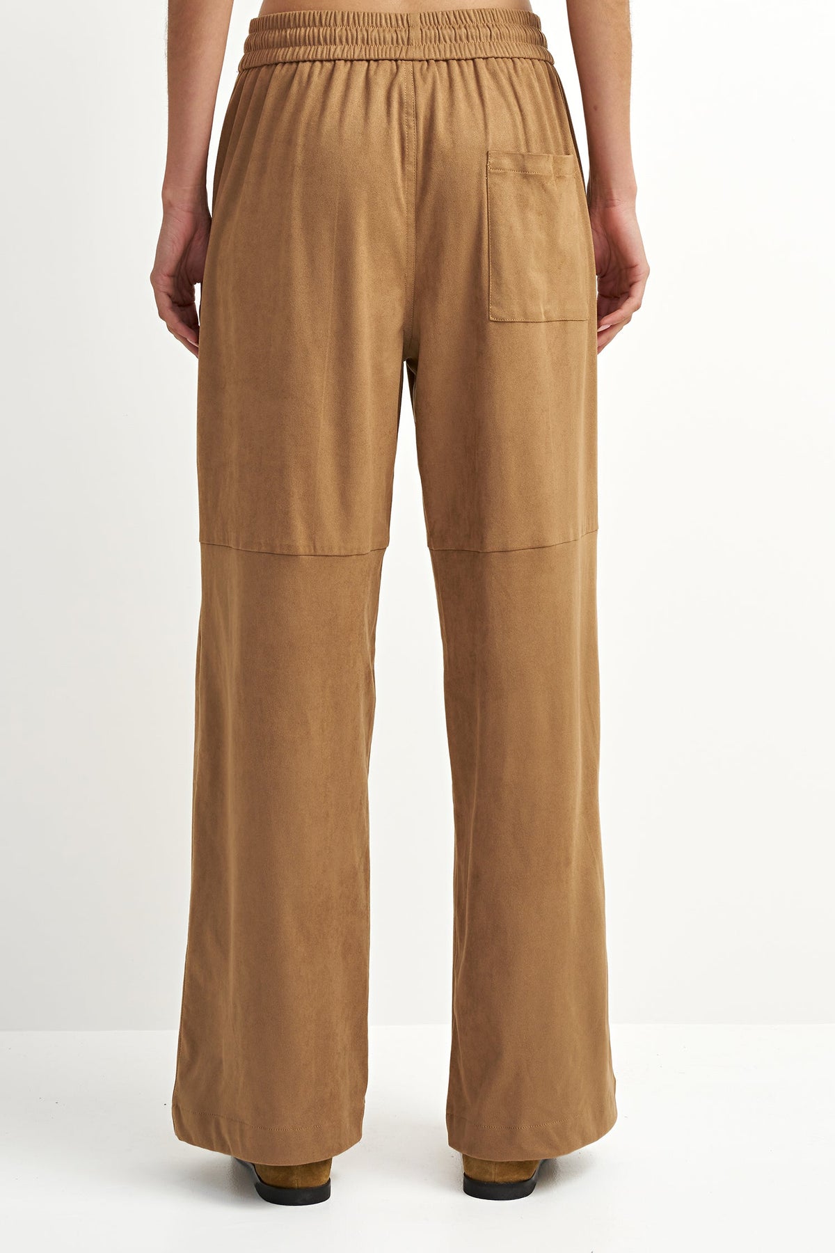 A person shown from the back wearing tan wide-leg pants with an elastic waistband, side pockets, and patch pockets on the upper legs, photographed against a plain light background.