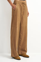 A person wearing wide-leg tan pants with an elastic waistband, drawstring, and side pockets, paired with tan shoes against a plain light background.
