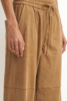 Close-up of a person wearing wide-leg tan pants with an elastic drawstring waistband and side pockets, shown against a plain light background.
