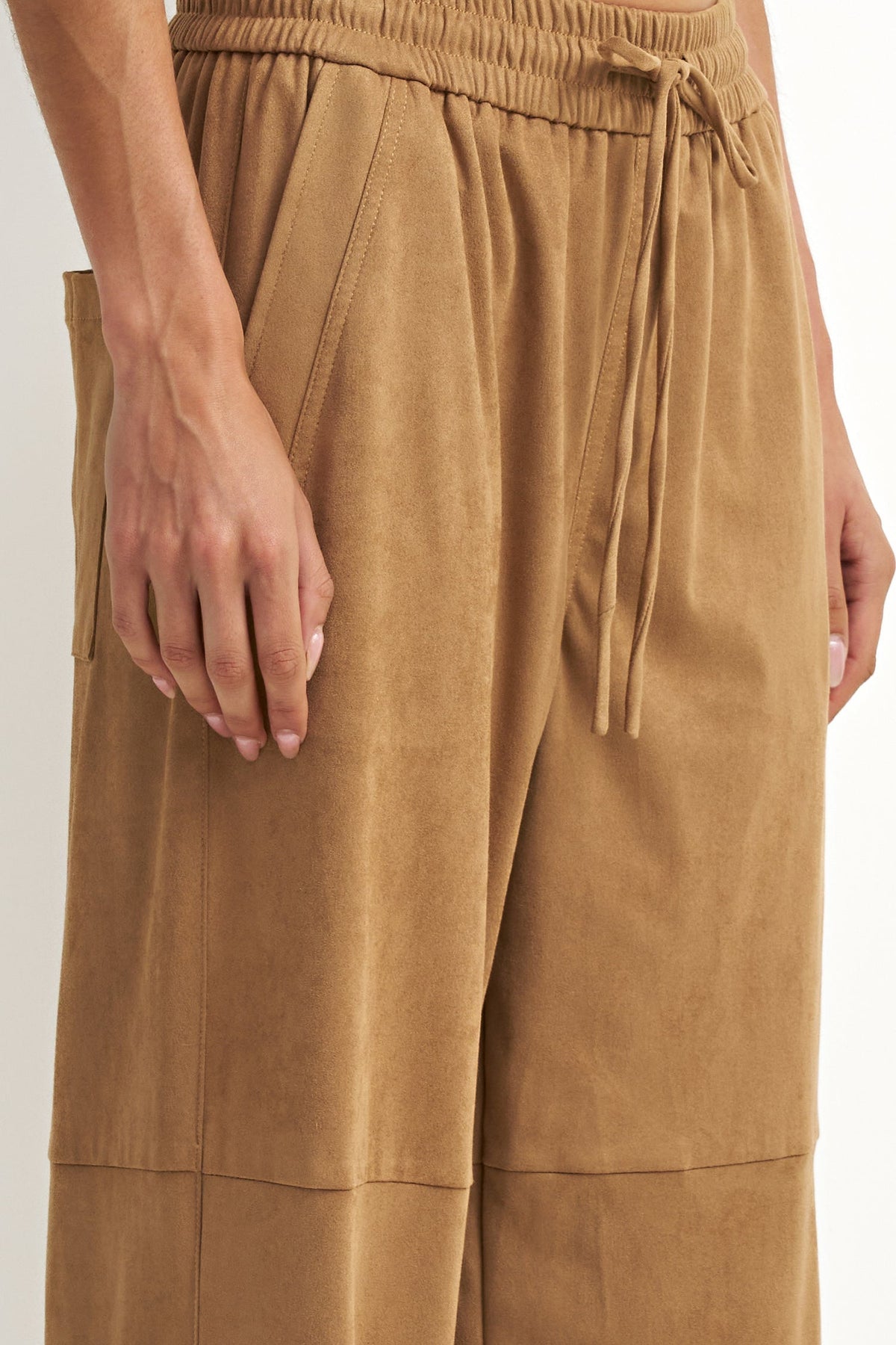 Close-up of a person wearing wide-leg tan pants with an elastic drawstring waistband and side pockets, shown against a plain light background.
