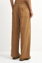 A person shown from the back wearing wide-leg tan pants with an elastic waistband, a side pocket, and patch pockets on the legs, photographed against a clean white studio background.