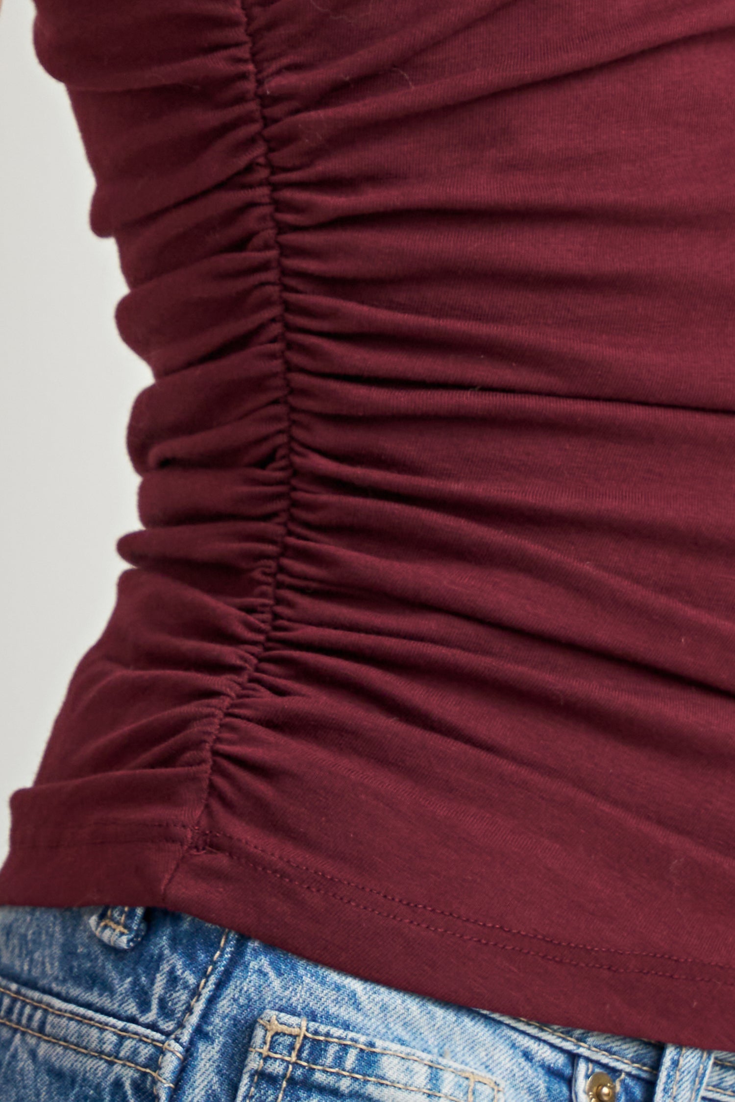 Close-up of a ruched scoop-neck top in deep burgundy, paired with blue denim jeans.