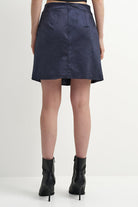A model shown from the back wearing a navy blue satin A-line mini skirt and black high-heeled ankle boots against a plain white studio background.