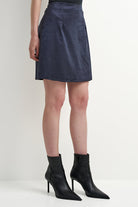 A model wearing a dark navy blue suede A-line mini skirt paired with black pointed-toe ankle boots with high stiletto heels, shown against a plain light gray studio background.
