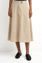 A model wearing a beige linen midi skirt with a button waistband, paired with black leather loafers, shown against a plain white studio background.