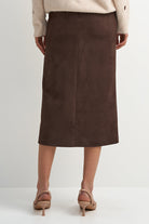 A model shown from the back wearing a dark brown midi skirt, a cream sweater, and beige heeled sandals against a light gray studio background.