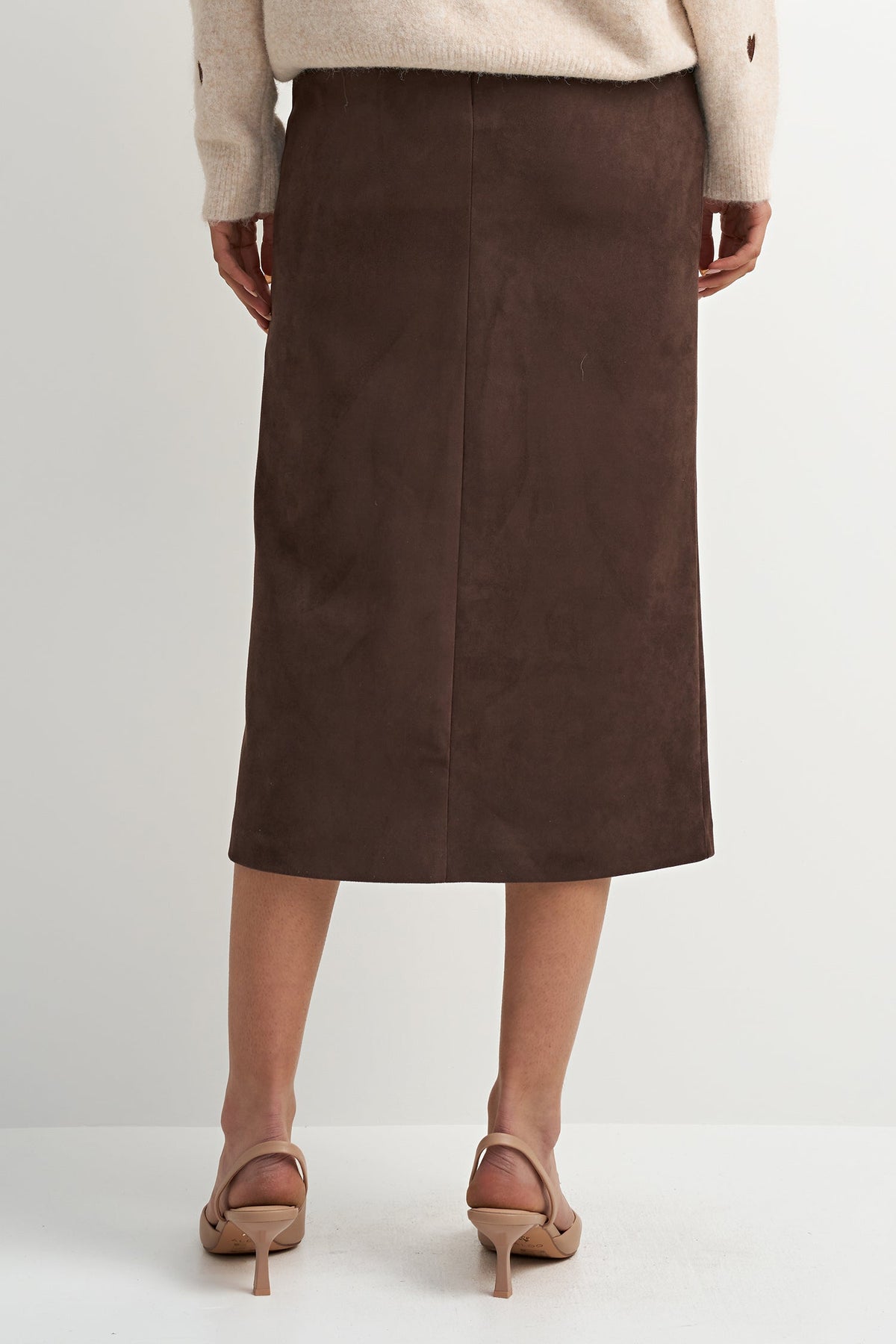 A model shown from the back wearing a dark brown midi skirt, a cream sweater, and beige heeled sandals against a light gray studio background.