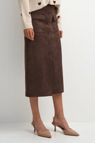 A model wearing a dark brown suede-look midi skirt with a button-front closure and flap pockets, styled with a cream knit sweater and beige slingback heels against a light gray studio background.
