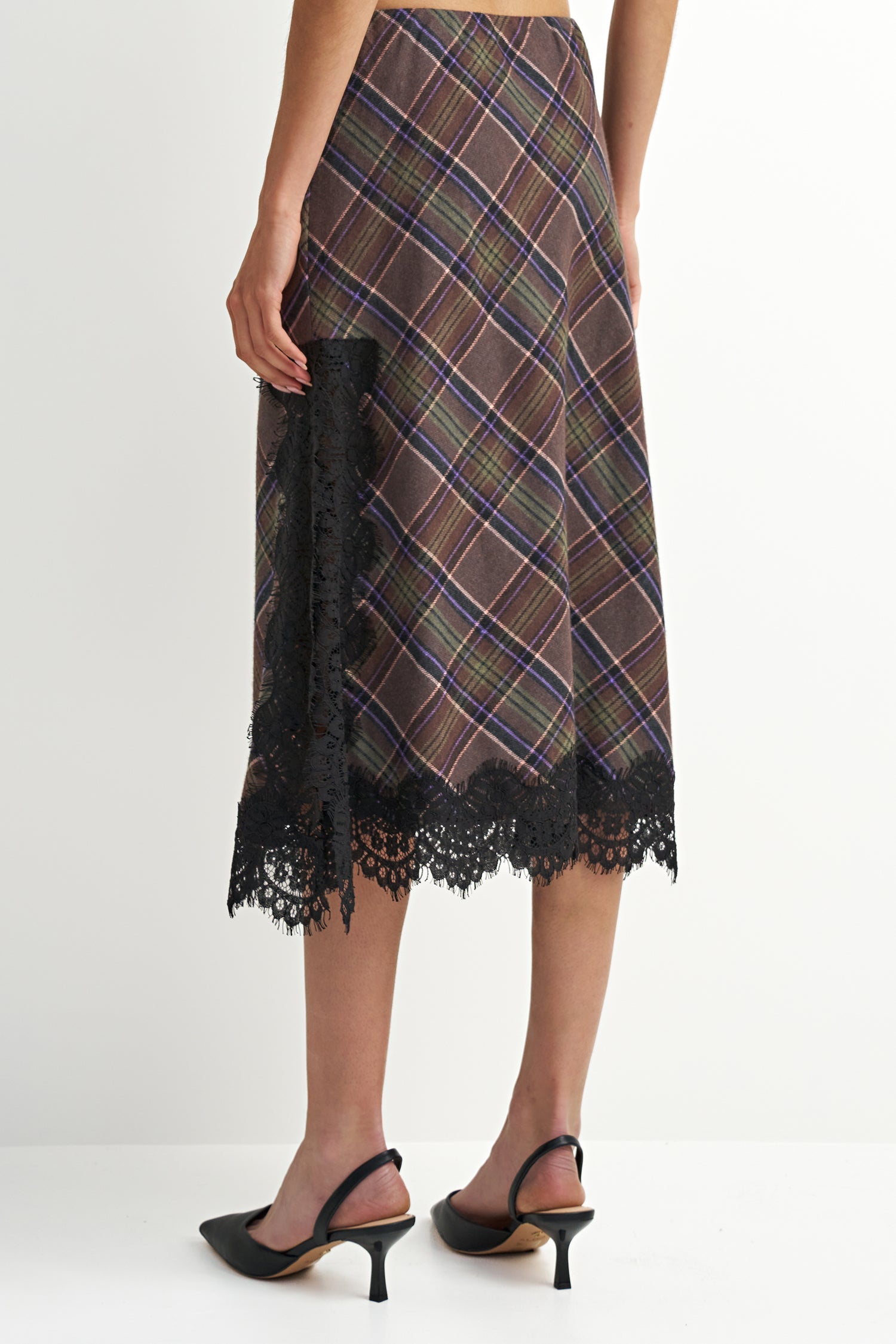 A model is shown from the back wearing a brown and navy plaid midi skirt with black lace trim, paired with black slingback heels.