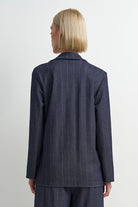 A model shown from the back wearing a navy blue pinstripe blazer and matching trousers against a plain white studio background.
