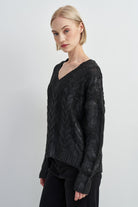 A woman modeling a black cable-knit V-neck sweater against a plain light gray studio background.