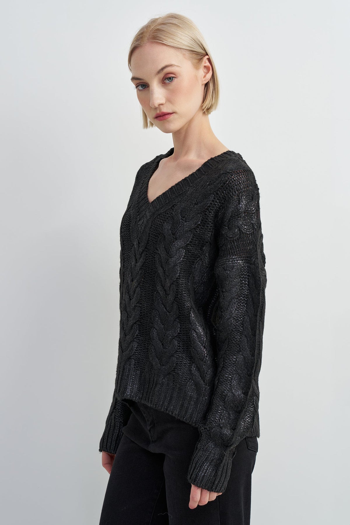 A woman modeling a black cable-knit V-neck sweater against a plain light gray studio background.