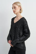 A blonde model wearing a black cable-knit V-neck sweater, shown from a side profile against a light gray studio background.