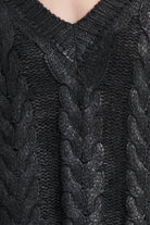Close-up of a black cable-knit sweater with a V-neck, showing detailed knit texture and braided patterns.