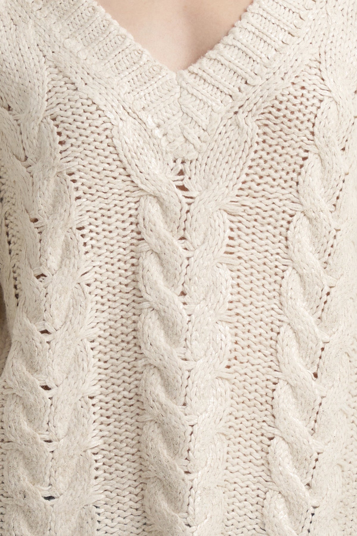 Close-up of a cream-colored cable-knit sweater with a V-neck, showing detailed knit texture and pattern.